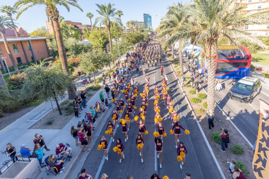 A top view of cheerleaders and ASU students marching down the street with pom poms waving up in the air for the parade