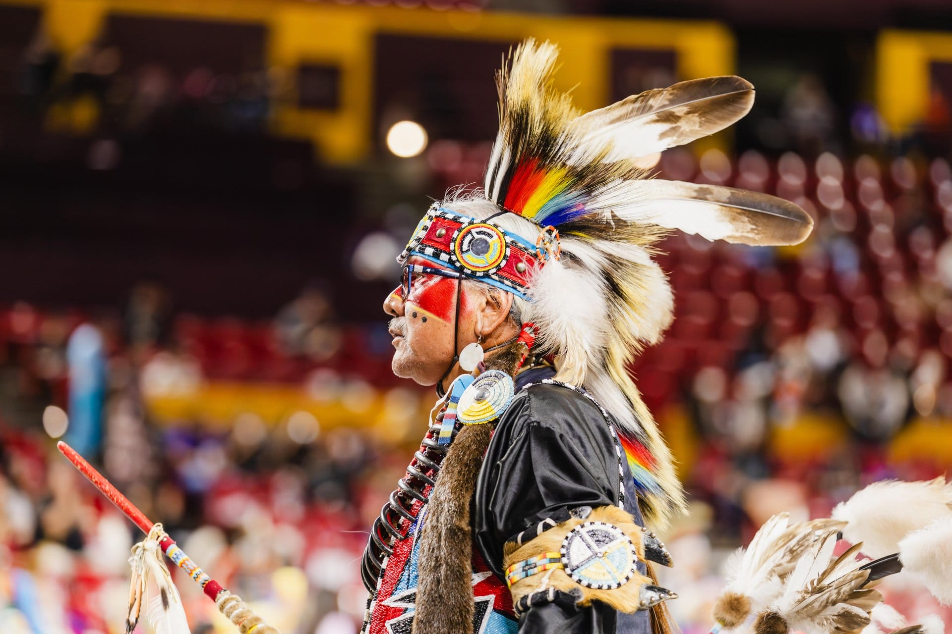Native American man in traditional regalia with feathers and beaded accessories