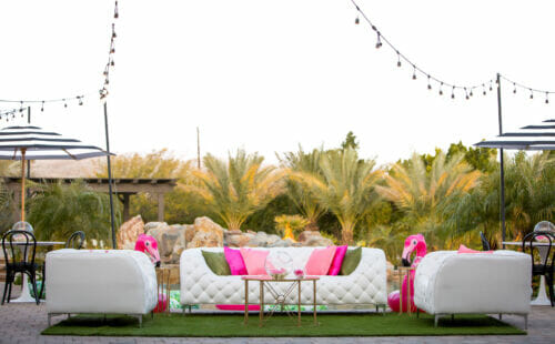 outdoor event set-up amidst palm trees with white couches, pink pillow
