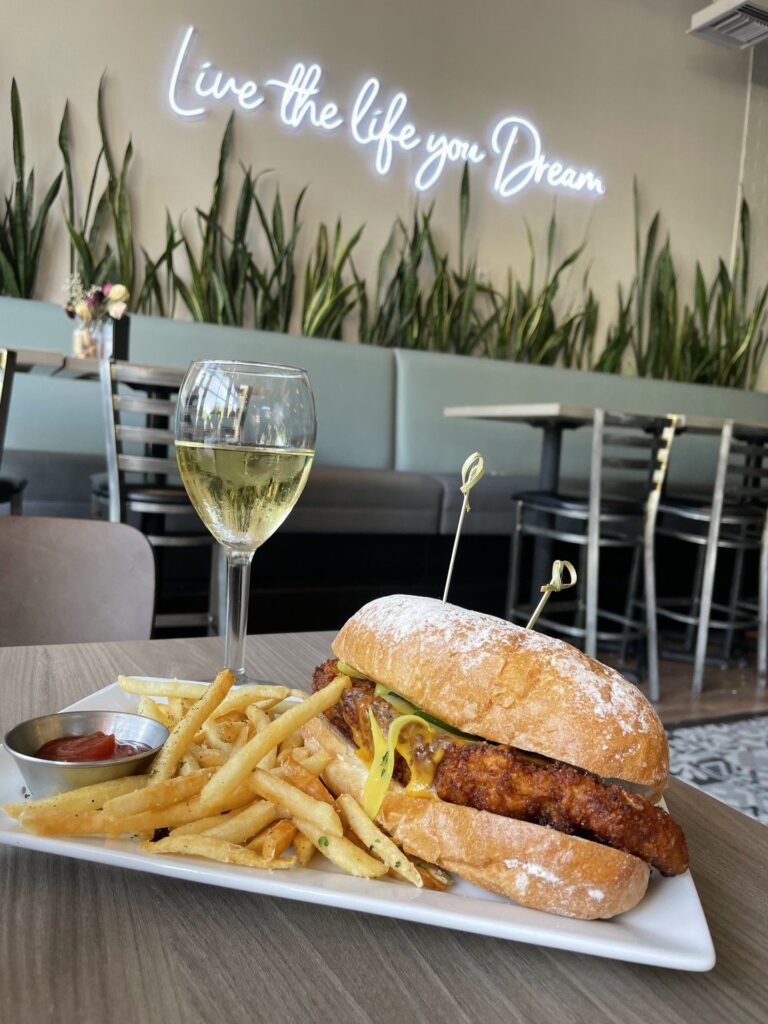 A chicken sandwich with fries and a glass of wine