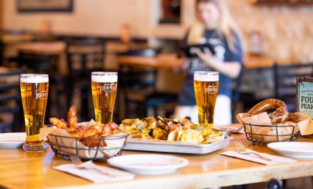 Three beers with a plate of nachos, pretzels and chicken tenders
