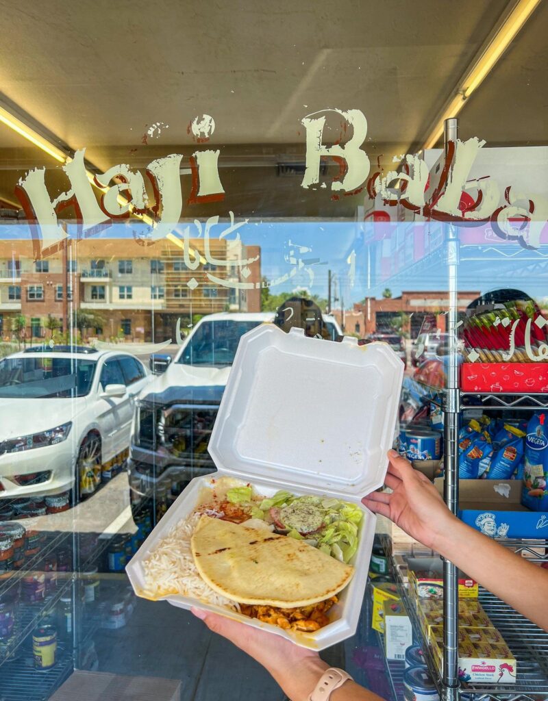 A take-out box with Mediterranean meal against a sign that says "Haji Baba"