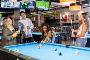 A girl playing billiards with three friends cheering her on