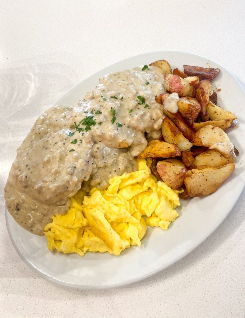 A plate of biscuits and gravy with a side of potatoes