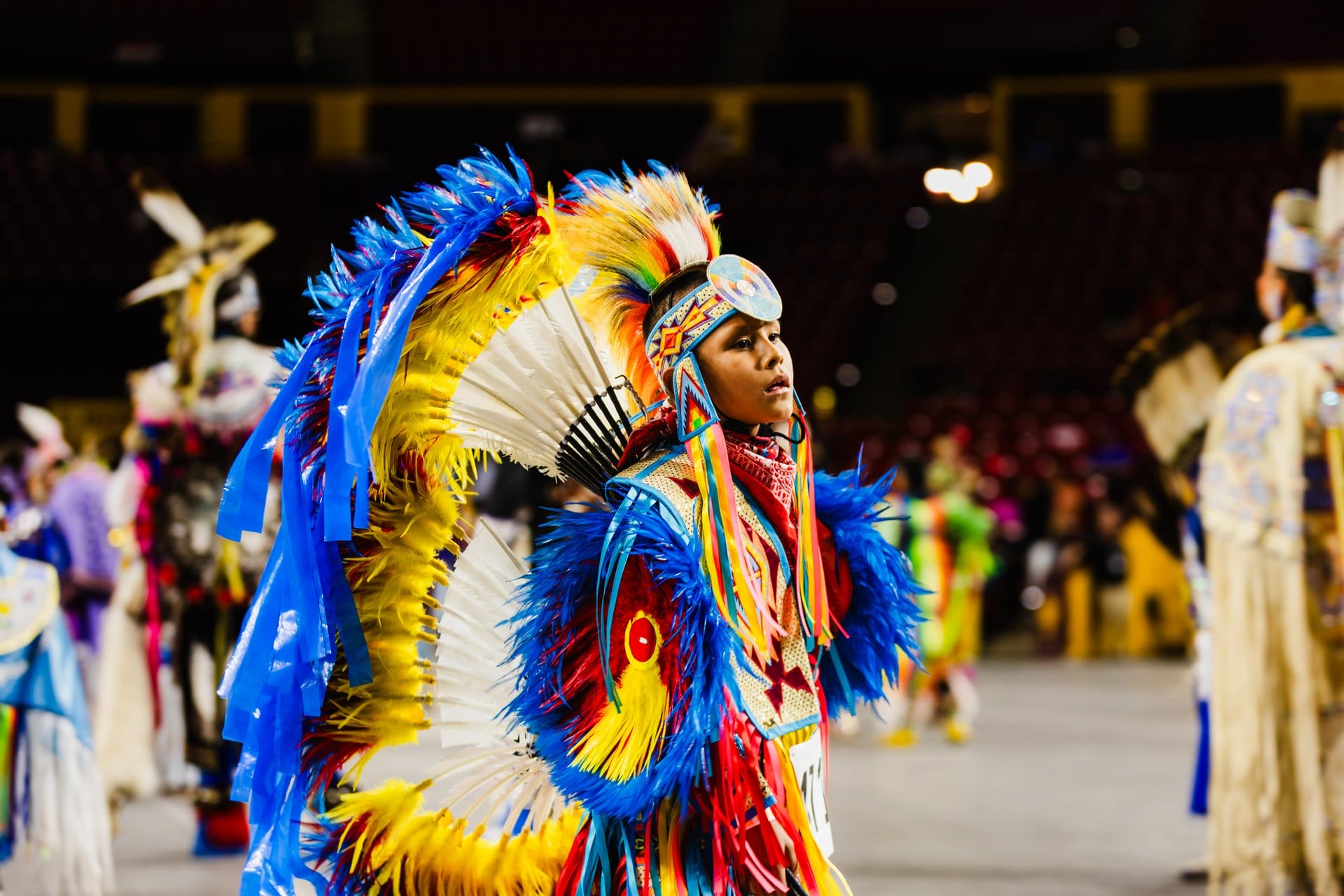 Young dancer wearing vibrant feathered regalia performs at Pow Wow at ASU.