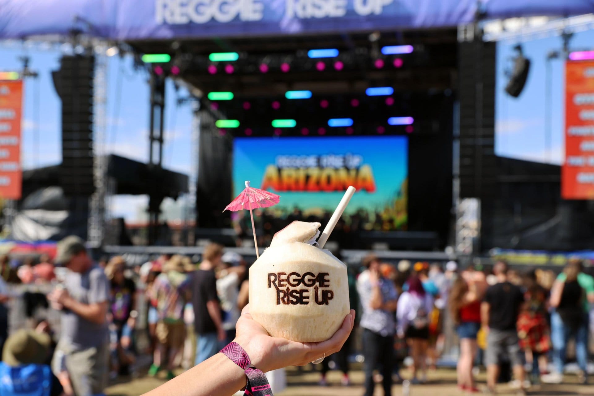 Branded coconut held up with Reggae Rise Up Arizona stage in background.