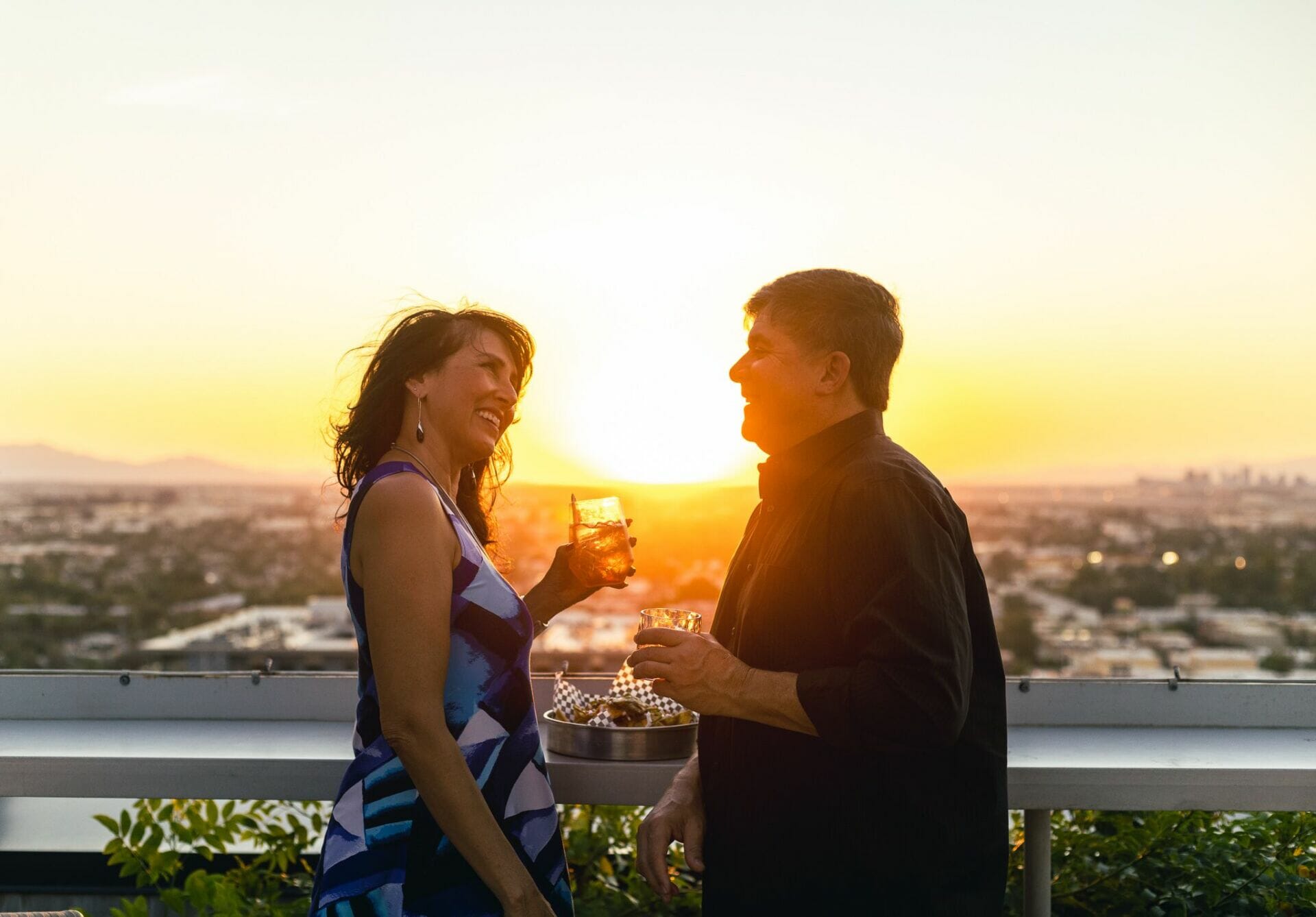 A couple wtih cocktail drinks on hand overlooking a sunset in Tempe