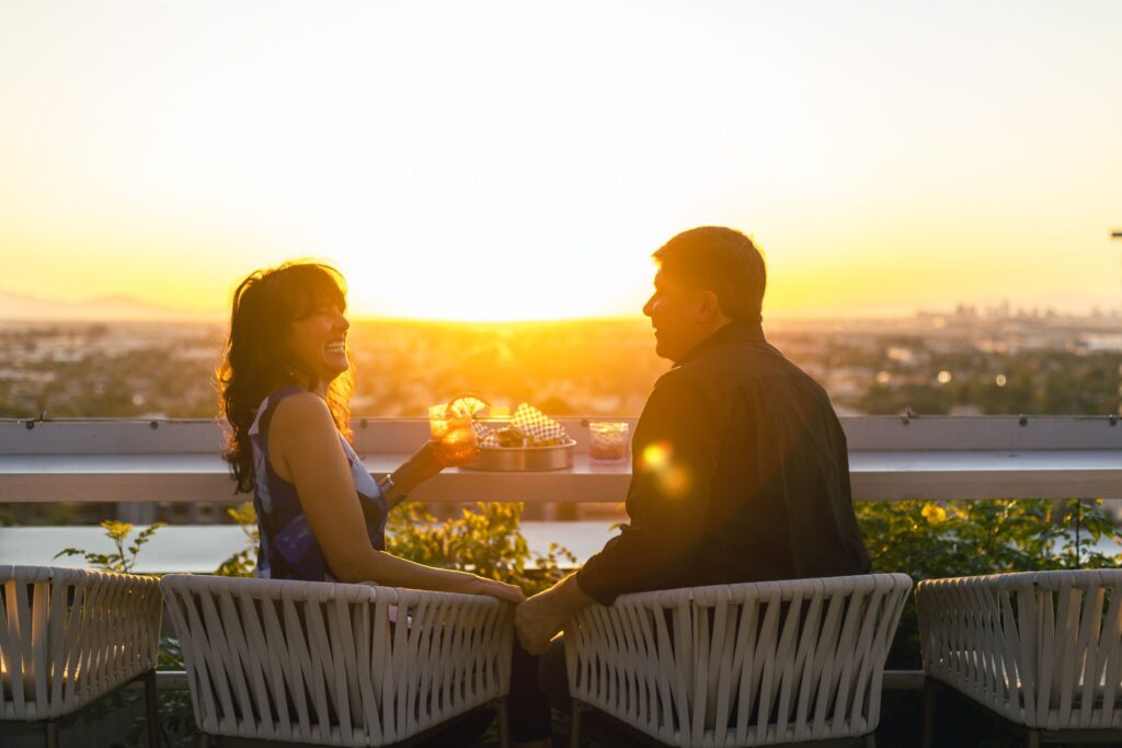 A couple wtih cocktail drinks on hand overlooking a sunset