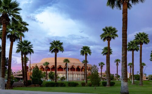 ASU Gammage with palm trees in the front and with a purple hue sunset in the background and