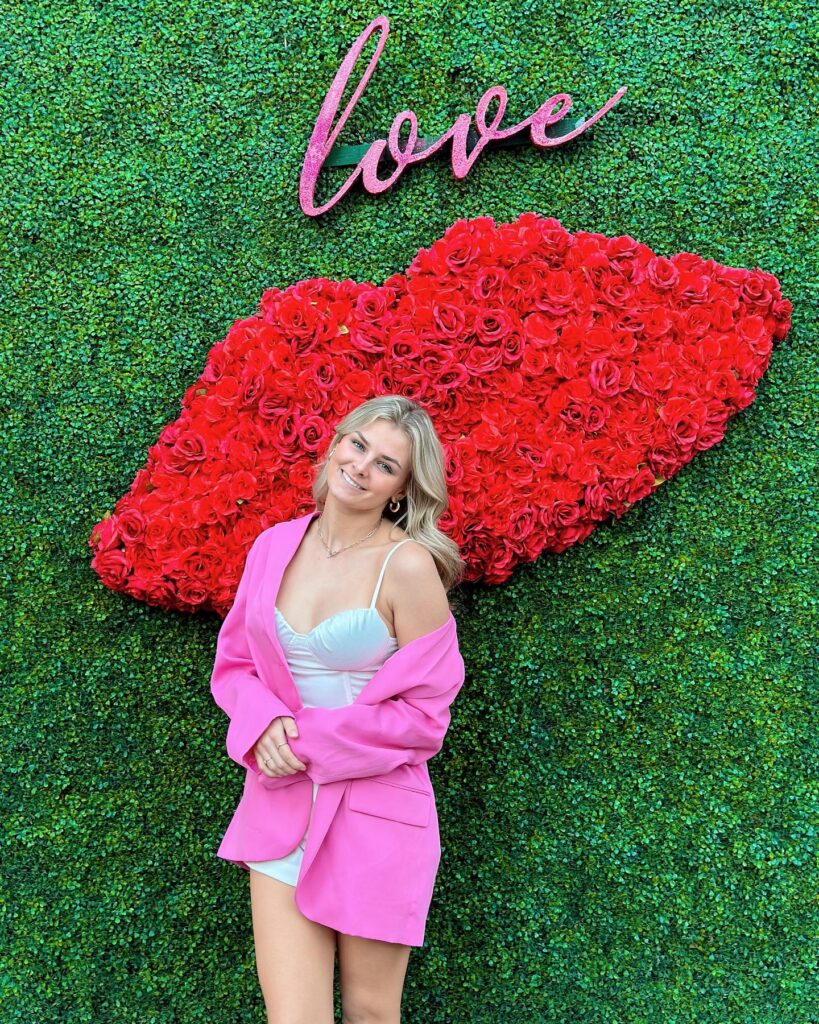 A smiling person stands in front of a lip-shaped floral installation at Tempe Marketplace/